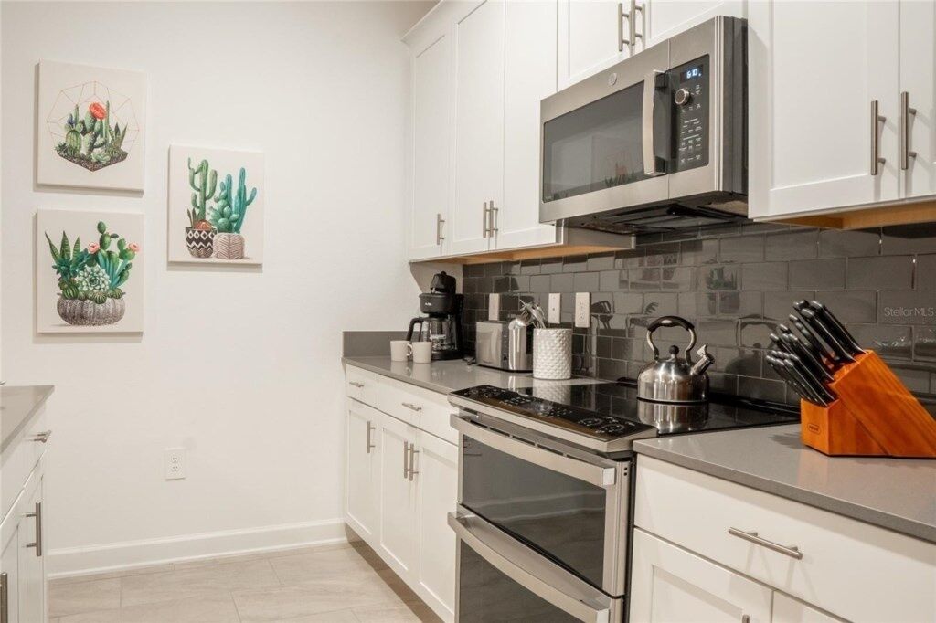 A modern kitchen with white cabinets, stainless steel appliances, and a microwave. There are three framed cactus artworks on the wall.