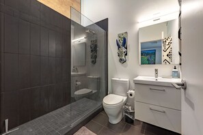 A modern bathroom with a glass-enclosed shower, a toilet, a sink with a mirror, and a decorative wall piece. - Happenstance Vineyards 2 Bedroom Home (Mosier)