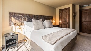 A neatly arranged bedroom with a large bed, a bedside table, a wall-mounted lamp, and a wooden door. - Copperbottom Inn 101 1 Bedroom Condo (Park City)