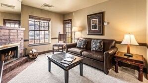 A cozy living room with a fireplace, a leather sofa, a coffee table, and a side table with a lamp. - Copperbottom Inn 101 1 Bedroom Condo (Park City)