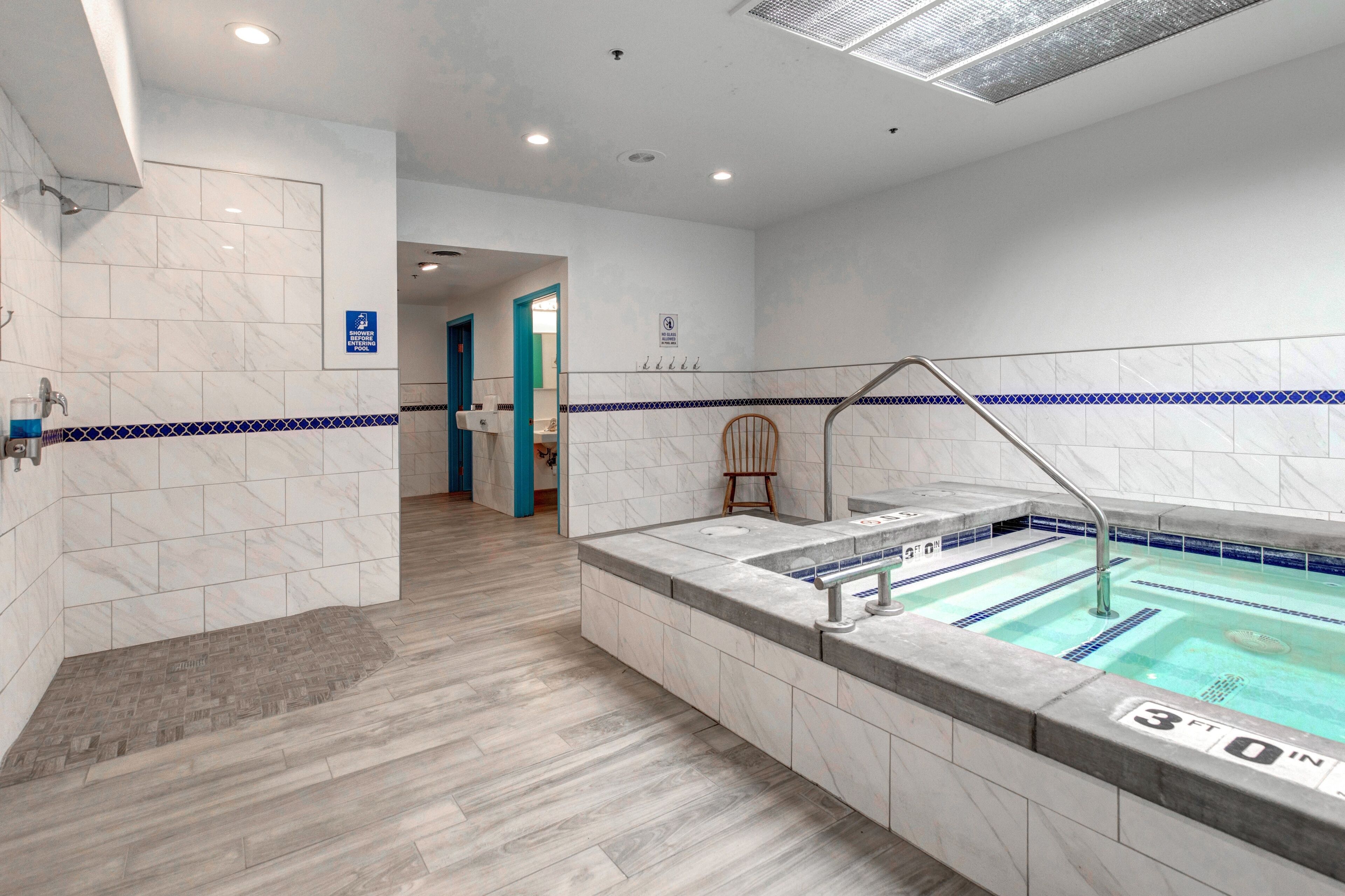 A modern bathroom with a marble floor, a small pool, and a blue-tiled border.