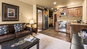 A modern kitchen with wooden cabinets, a refrigerator, microwave, and a stove. There is a dining area with a table and chairs. - Copperbottom Inn 101 1 Bedroom Condo (Park City)