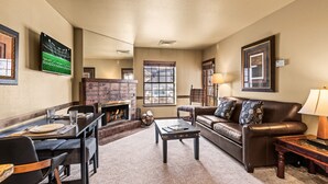 A living room with a fireplace, a leather sofa, a dining table with chairs, and artwork on the walls. - Copperbottom Inn 101 1 Bedroom Condo (Park City)