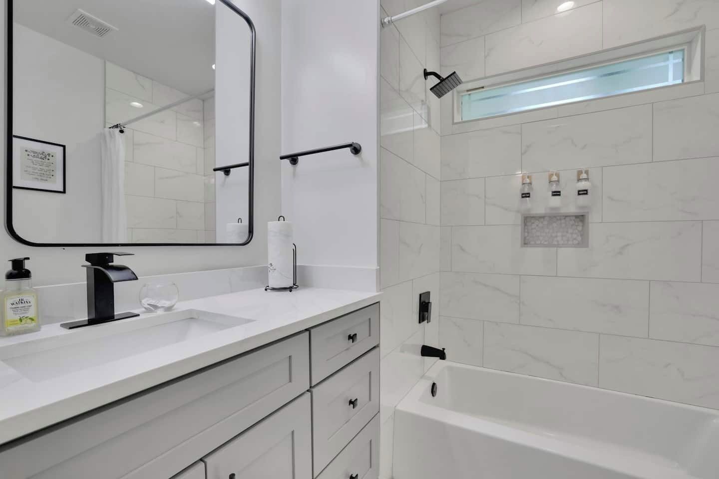 Ein modernes Badezimmer mit einem weißen Marmorwaschbecken, einem großen Spiegel, einer Handbrause und einer integrierten Badewanne.