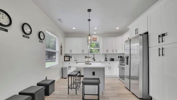 A modern kitchen with white cabinets, a central island with stools, and a stainless steel refrigerator. - Haven Hideway Atlanta Downtown (Atlanta)
