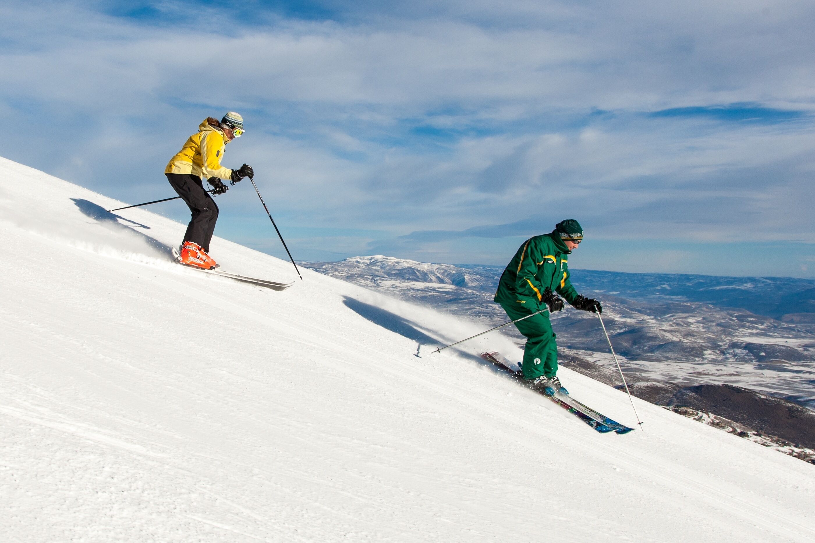 Twee skiërs op een besneeuwde helling onder een heldere lucht.