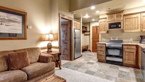 A compact living space with a sofa, a coffee table, a lamp, a refrigerator, a microwave, an oven, and wooden cabinets. - Copperbottom Inn 311 1 Bedroom Condo (Park City)