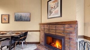 A dining area with a brick fireplace, framed artwork on the wall, and a table set for two. - Copperbottom Inn 311 1 Bedroom Condo (Park City)
