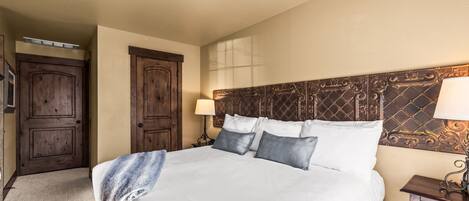A hotel room with a large bed, wooden headboard, and a nightstand with a lamp.