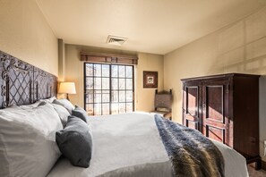 Una cama bien hecha con cabecera, una ventana con persianas, un armario de madera y un cuadro en la pared.