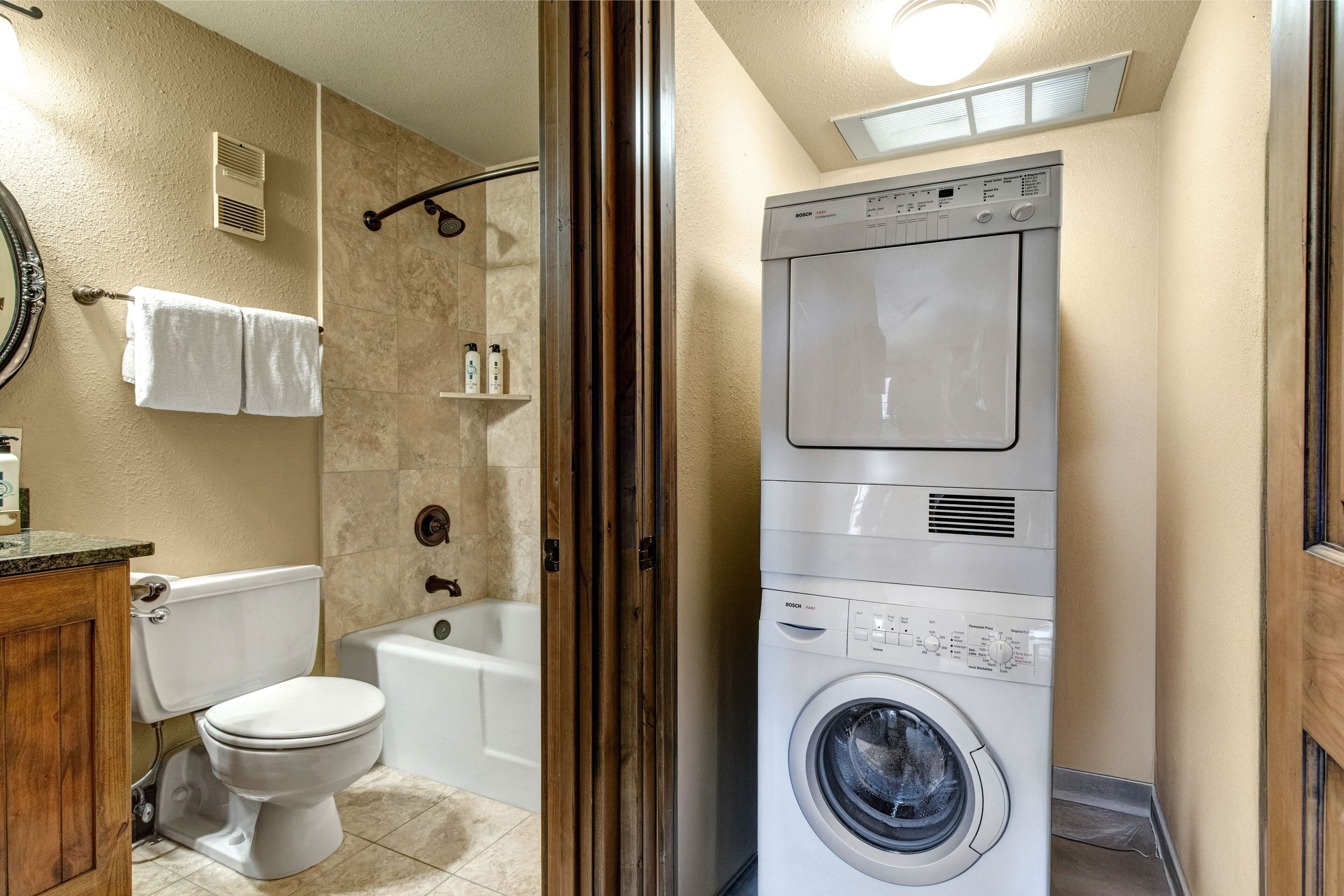 A laundry room with a stacked washer and dryer, a toilet, and a bathtub.