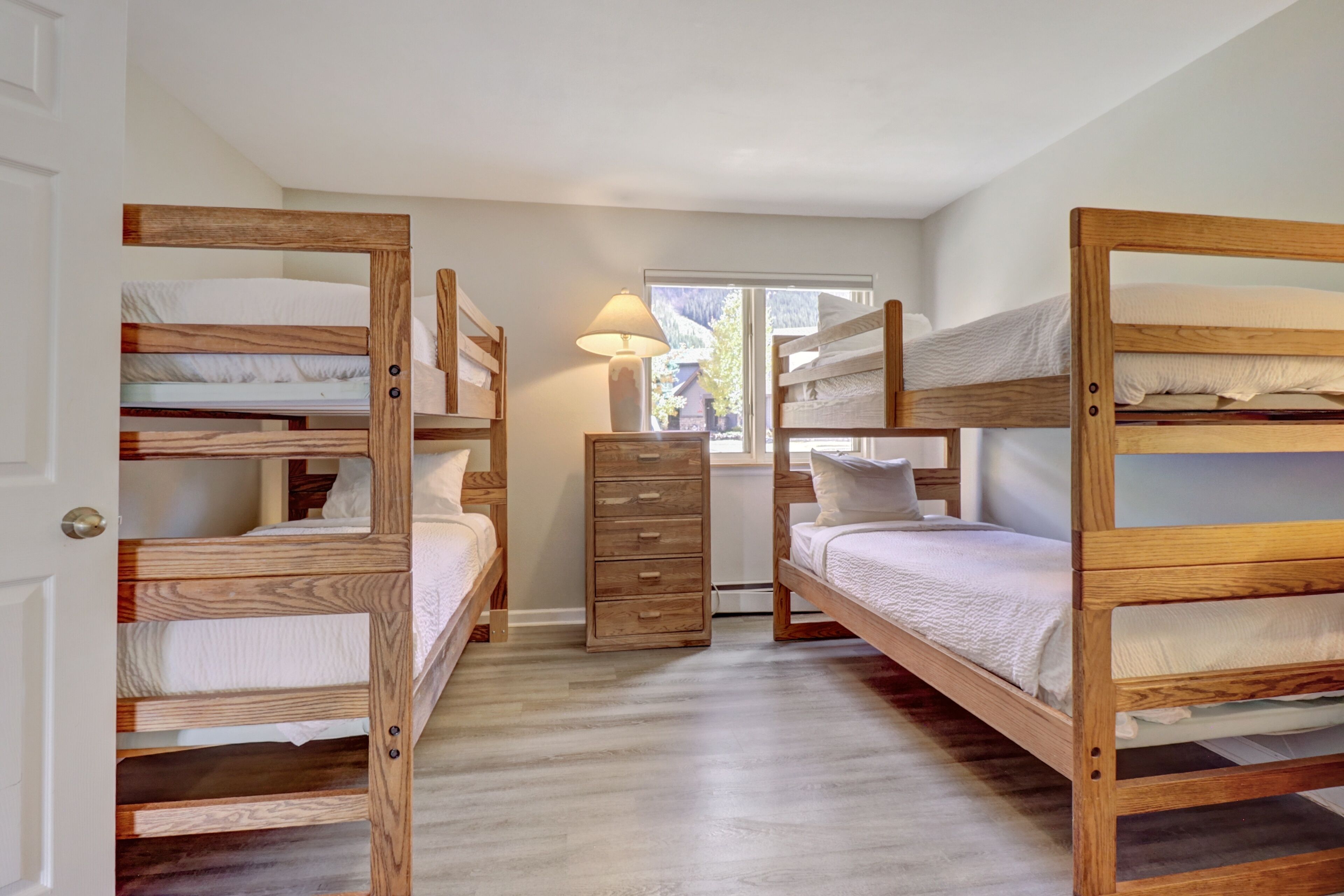 Ein Zimmer mit drei Etagenbetten, einer Holzkommode und einem Fenster mit Lampe.