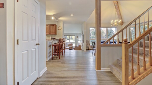 A spacious living area with a wooden staircase, a kitchen in the background, and a dining area with chairs and a table. - Legends 11 5 Bedroom Townhouse (Copper Mountain)