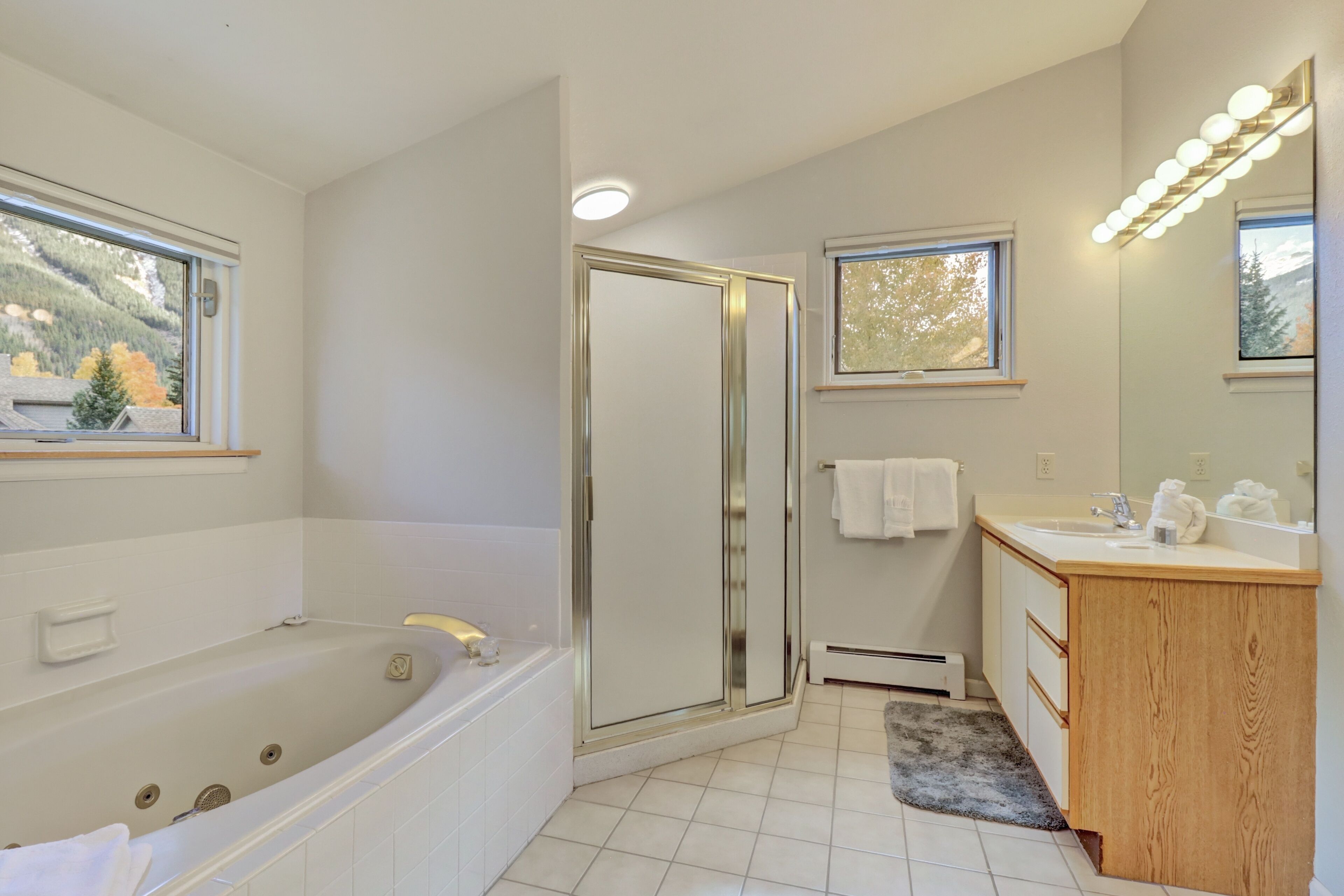 A modern bathroom with a bathtub, shower, vanity, and a large mirror with lights.