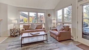 A spacious living room with two beige sofas, a wooden coffee table, and a large window offering a view of a mountainous landscape. - Legends 11 5 Bedroom Townhouse (Copper Mountain)