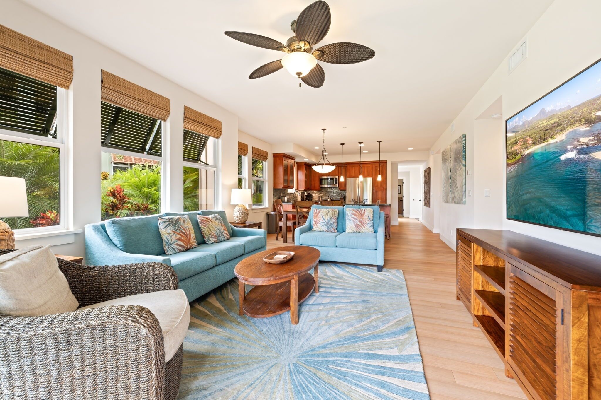 Un ampio soggiorno con un'ampia televisione, un ventilatore a soffitto e una cucina sullo sfondo.
