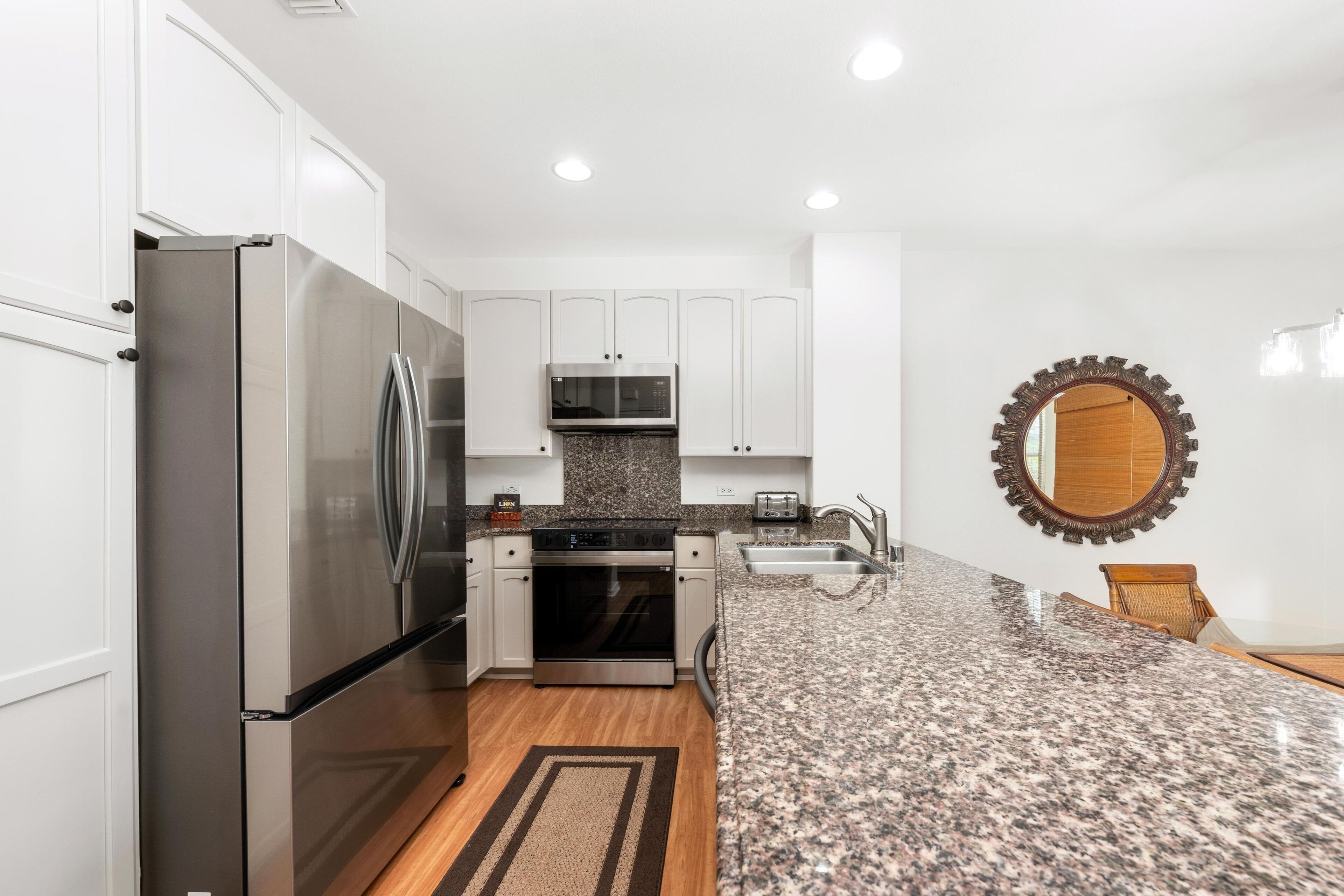 A modern kitchen with white cabinets, stainless steel appliances, granite countertops, and a wooden floor.