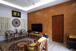 Een woonkamer met een televisie, houten meubels, een vloerkleed met dessin en een grote deur.