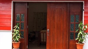 A wooden door with glass panels, a potted plant on the left, and another on the right. - Voon Cottages@Pinjistation Private Pool 10pax (Ipoh)