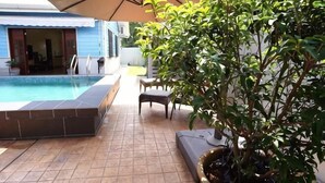 A swimming pool with a tiled edge, a patio area with a table and chairs, and a large umbrella providing shade. - Voon Cottages@Pinjistation Private Pool 10pax (Ipoh)