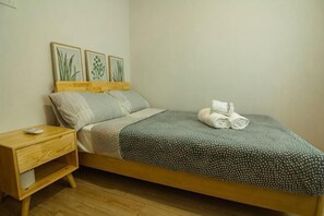 Un lit simple avec un cadre en bois, une table de chevet avec une lampe et une œuvre d’art accrochée au mur.