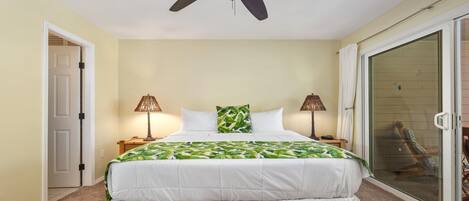 A bedroom with a bed, two bedside lamps, a ceiling fan, a sliding glass door, and a chair outside.