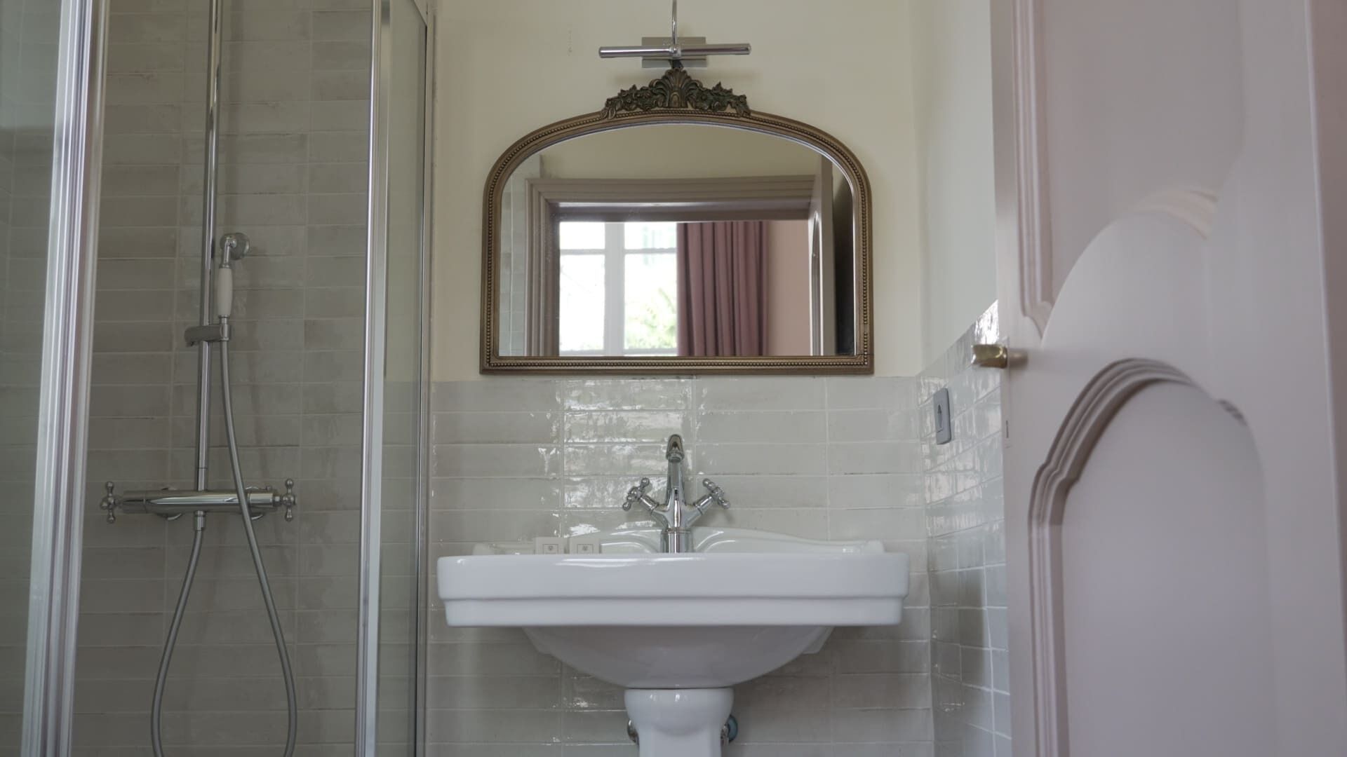 A bathroom with a glass shower enclosure, a white sink, and a mirror with an ornate frame.