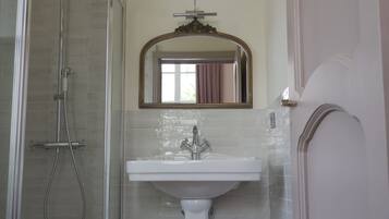 Un baño con cabina de ducha de vidrio, un lavamanos blanco y un espejo con un marco decorativo.