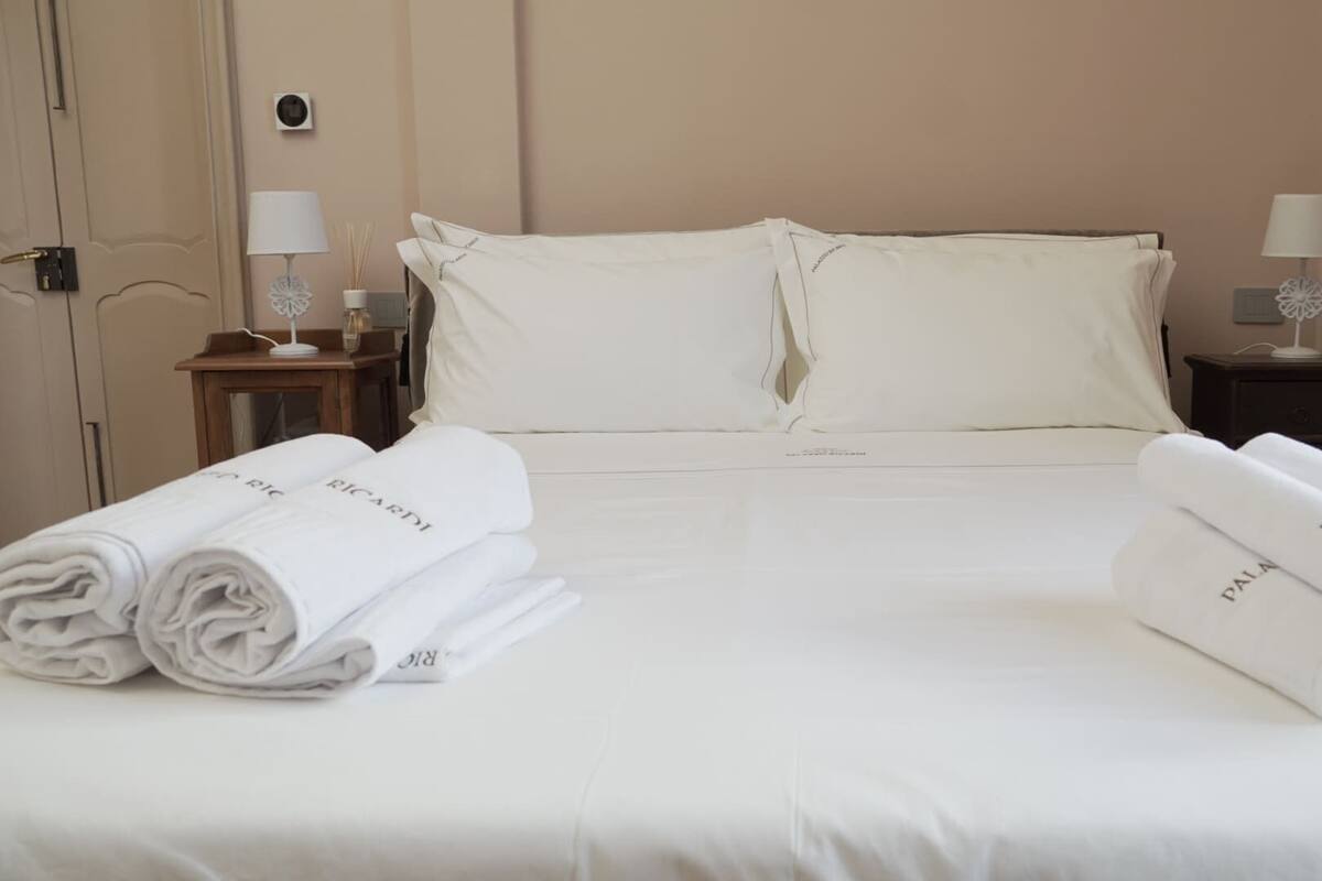 A neatly made bed with white linens and rolled towels labeled "RICARDI" and "PAUL".