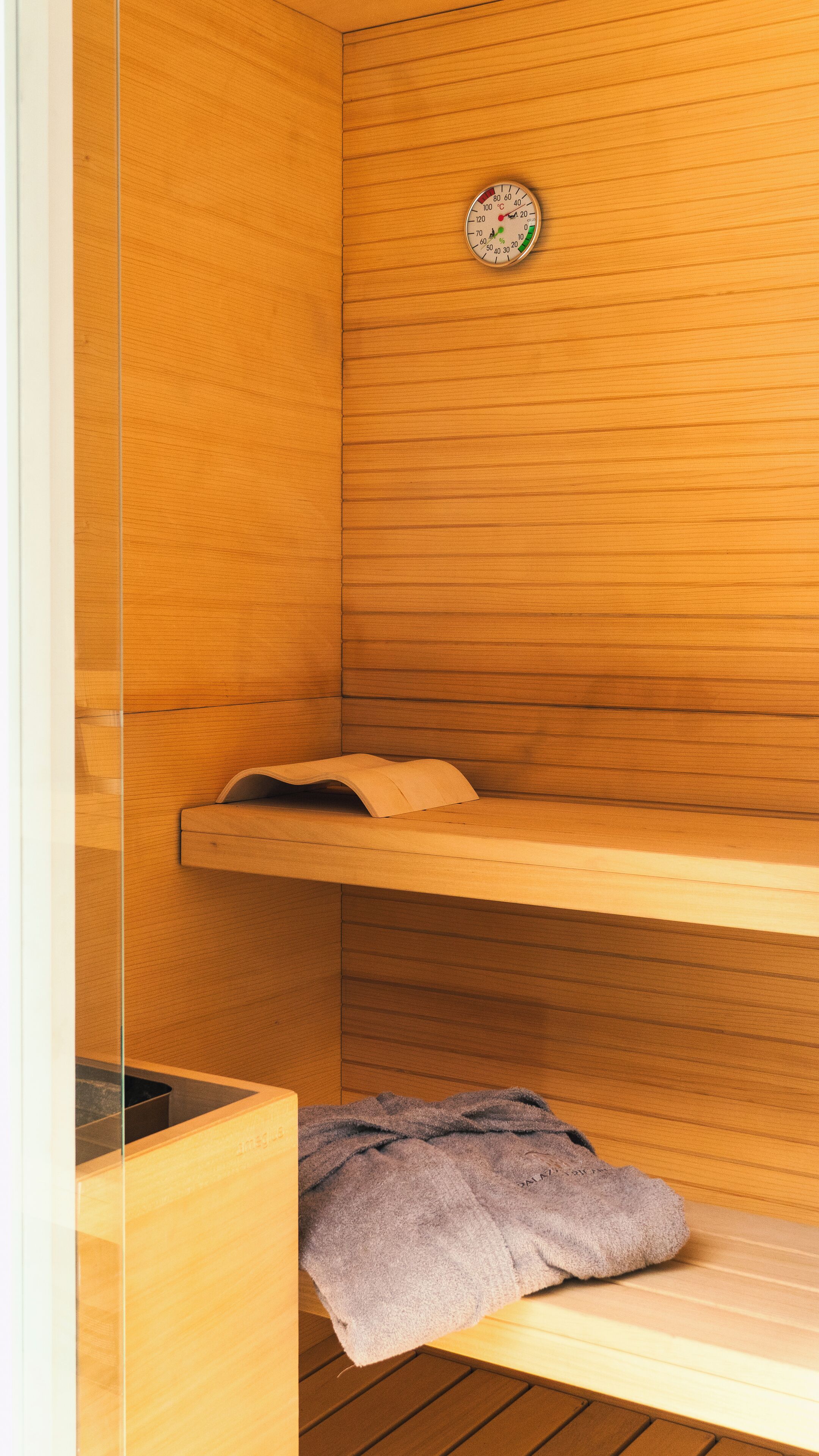 Une salle de sauna avec des murs en bois, un thermomètre et une serviette sur le sol.