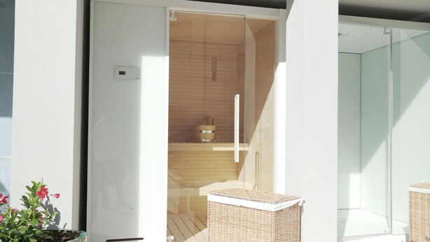 A modern bathroom with a glass shower enclosure, a wooden bench, and a visible thermostat. - PALAZZO RICARDI (Imperia)