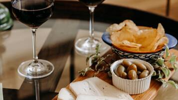 Une planche en bois garnie de fromage, de charcuterie, d’olives et d’un bocal de noix. On peut également apercevoir deux verres de vin rouge.
