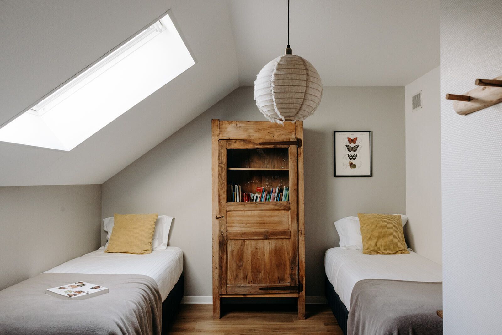 Une chambre avec deux lits, une lucarne, une bibliothèque en bois et une décoration murale représentant des papillons.