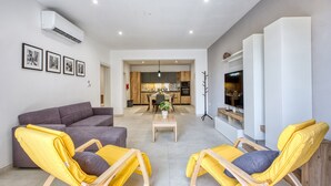 A modern living room with a grey sofa, yellow chairs, a coffee table, and a kitchen in the background. - Spacious & Cozy 4-Bedroom in Sliema JELL1-2 (Sliema)