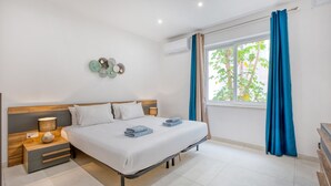 A neatly made bed with a wooden headboard, a bedside table with a lamp, and a wall-mounted decorative item. - Spacious & Cozy 4-Bedroom in Sliema JELL1-2 (Sliema)