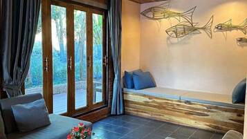 Una habitación con sofá, una mesa de centro de vidrio con flores, un banco y una pared decorada con arte abstracto de peces.