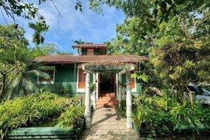 Una casa con tejado de paja, rodeada de abundante vegetación y un sendero que lleva a la entrada.