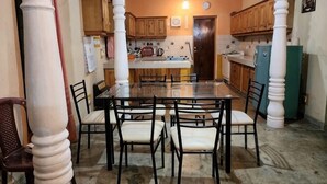 A dining area with a glass table surrounded by chairs, wooden cabinets, and a refrigerator. - Marakolliya Stay, 2BR Residential Holiday Bungalow (Hambantota)