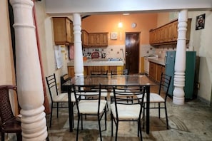 A dining area with a glass table surrounded by chairs, wooden cabinets, and a refrigerator. - Marakolliya Stay, 2BR Residential Holiday Bungalow (Hambantota)
