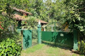 A gated entrance with a metal gate, a house with a red roof, and surrounding greenery.