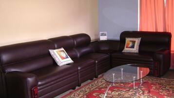 A living room with a dark brown leather sofa, a glass coffee table, and a patterned rug.