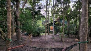 A hammock in a wooded area with trees and a building in the background. - Marakolliya Stay, 2BR Residential Holiday Bungalow (Hambantota)