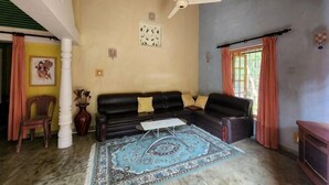 A living room with a black sofa, a patterned rug, a ceiling fan, and a window with curtains. - Marakolliya Stay, 2BR Residential Holiday Bungalow (Hambantota)