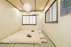 A room with tatami mats, a bed with pillows, a hanging light fixture, a window with a grid pattern, and an air conditioning unit. - Luxury Stay in Tokyo!4-minute walk from Hirai Station 100 Hideaway 2 Bath 3 Toilet (Tokyo)