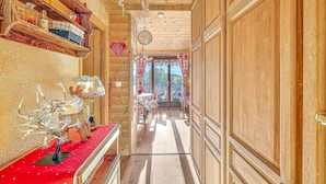 Un interior de madera con un pasillo que conduce a un comedor, estanterías con objetos y un árbol decorativo.