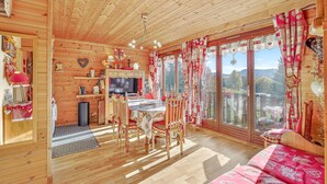 Interior de una cabaña de madera con comedor, sofá y vistas amplias por grandes ventanas.