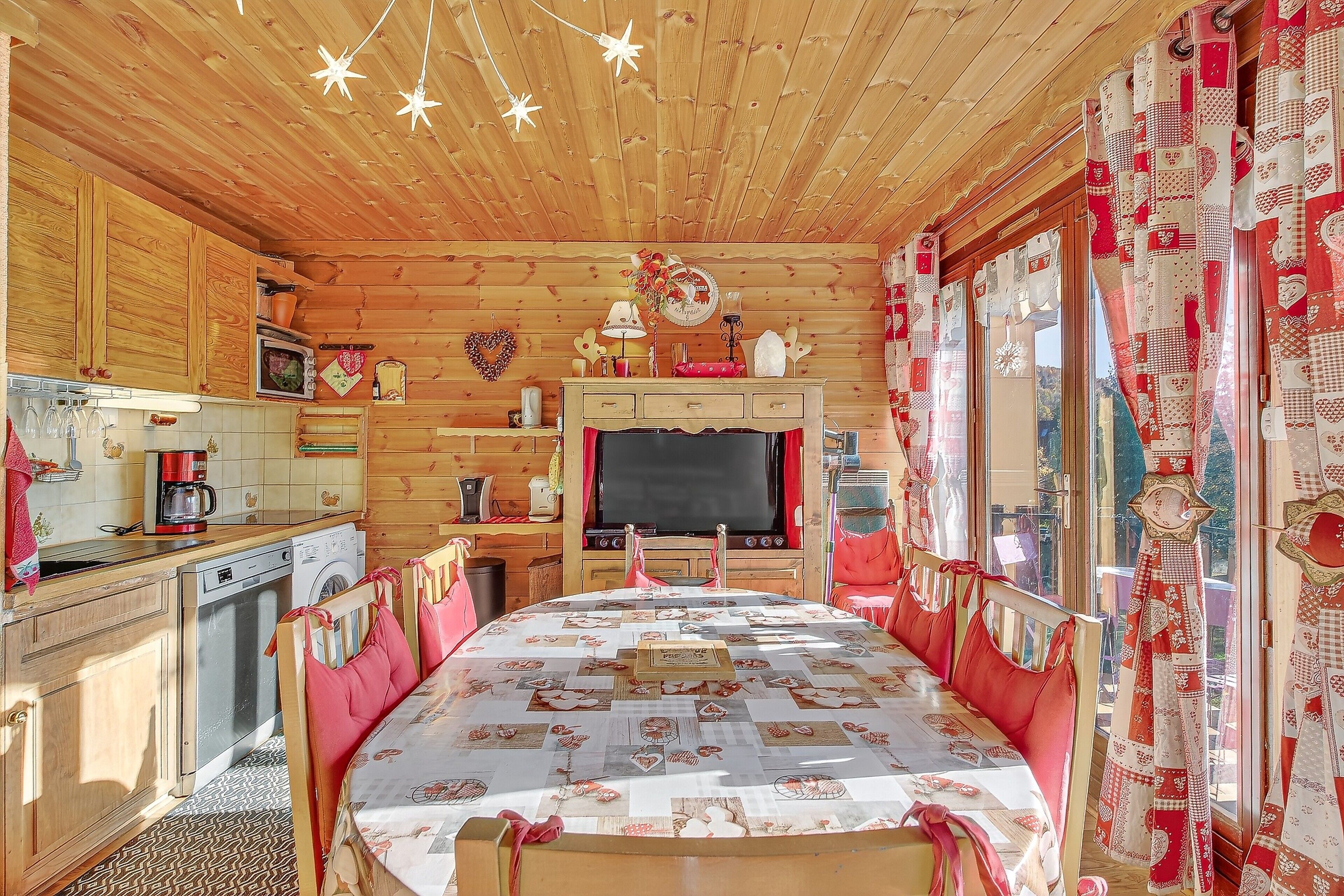 A cozy cabin interior with a dining table, wooden cabinets, a washing machine, and a television.