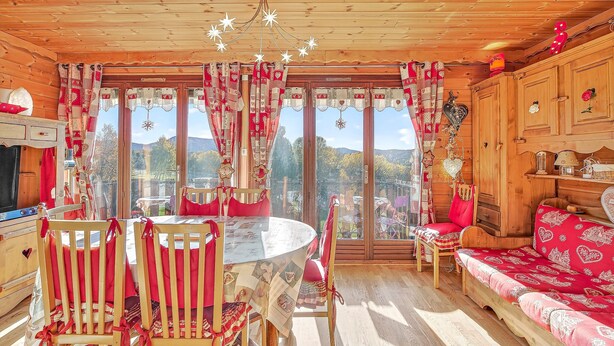 Un interior de madera con una mesa redonda, sillas, un sofá y vistas al exterior.
