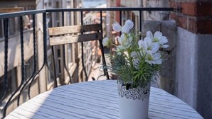 A round table with a white lace-patterned vase containing white flowers, set on a balcony with a wooden chair and metal railing. - Ganbaru Tours - Private Triplex&Duplex (Istanbul)