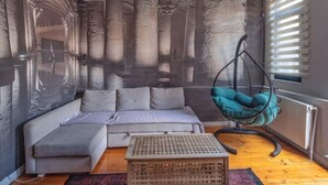 A modern living room with a grey sofa, a hanging teal chair, and a wooden crate. - Ganbaru Tours - Private Triplex&Duplex (Istanbul)